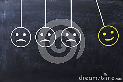 Spread happiness concept with happy and sad faces on newtonâ€™s cradle on blackboard Stock Photo